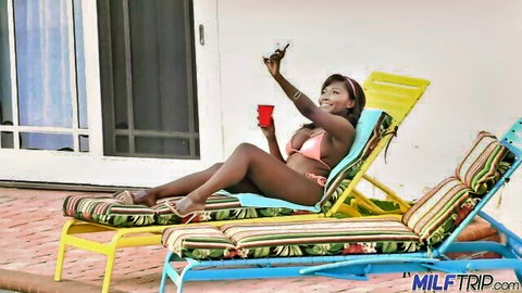 Thick ebony MILF in skimpy pink bikini lounges poolside taking selfie with big tits and curves