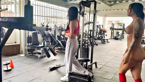 Tattooed nude Latina with huge ass and red stockings struts in gym beside brunette dropping white pants exposing curves