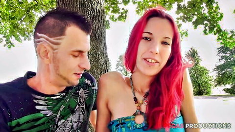 Smiling redhead teen in sexy top cuddles shaved-head guy outdoors by tree