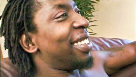 Smiling ebony man with dreadlocks shirtless grinning seductively on leather couch