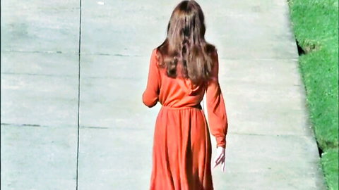 Annette Haven in flowing orange dress walking in retro porn classic