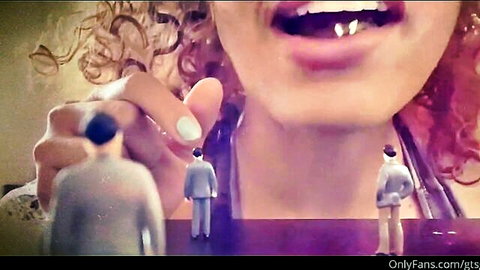 Ebony giantess with curly hair holds tiny suited men near open mouth in vore scene