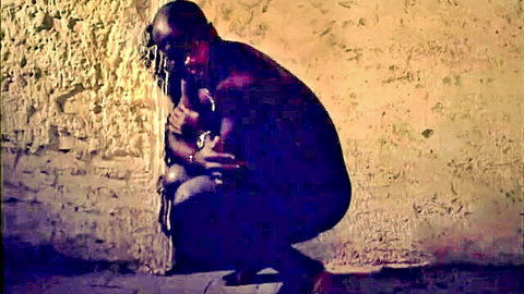 Muscular bald black man squats pants down groping woman's tits against rough brick wall in vintage scene