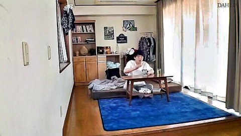 Japanese housewife in white blouse sits drinking tea at low table in sunny apartment room