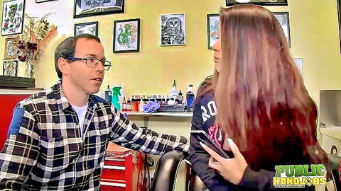 Redhead in hoodie touches guy's lap in tattoo parlor during public handjob tease