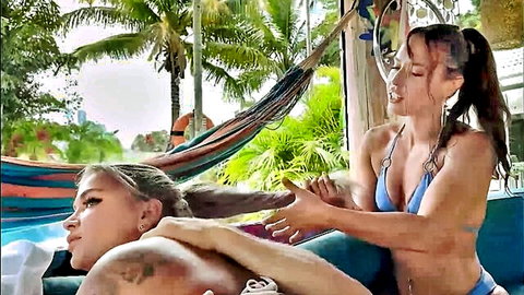 Two blonde women in bikinis by the pool, one massaging the other sensually