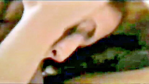 Close-up of blonde woman's pierced ear and pale skin in dim erotic lighting.