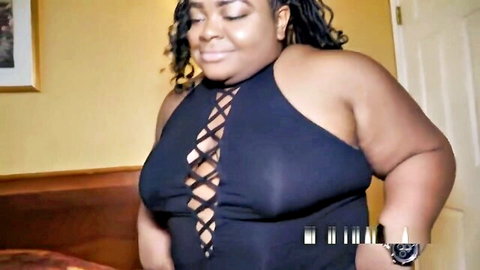 Smiling curvy BBW ebony woman in tight black lace-up dress showing deep cleavage