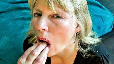Mature blonde housewife opens mouth with tongue out to lick thick cum from hand