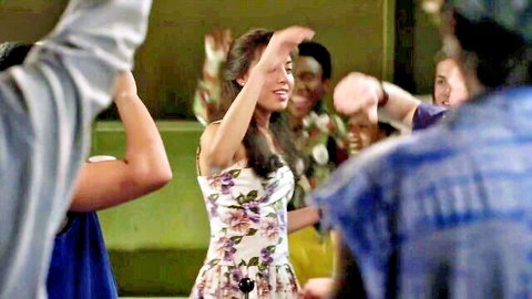 Smiling woman in floral dress raises arms dancing with group in lively club party