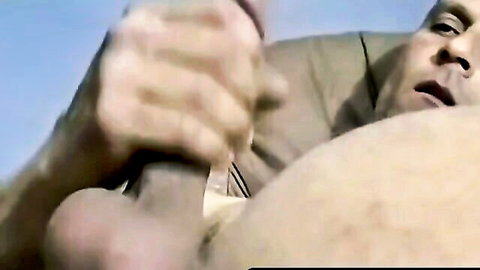 Muscular hand gripping and stroking massive erect cock in close-up gay handjob.