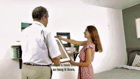Young brunette in short pink dress helped by older man to hang picture