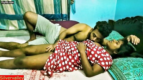 Desi MILF in red polka dot dress embraced by shirtless man in intimate bedroom scene