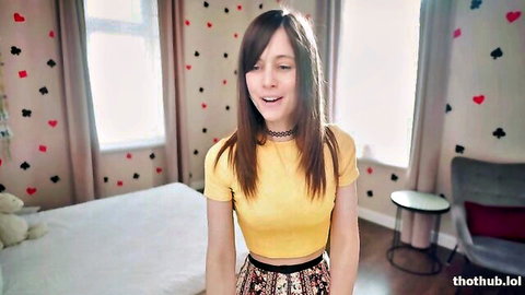 Brunette teen smiling in tight yellow crop top and colorful skirt on webcam striptease tease