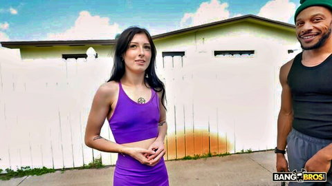 Kiki Mink in tight purple sports bra with black stud outdoors, smiling tease