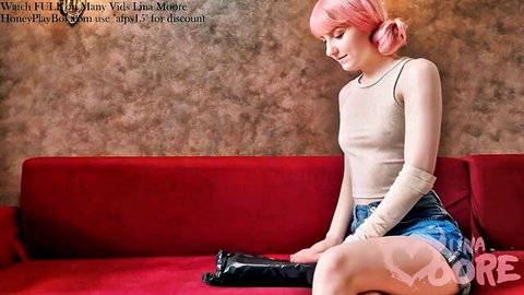 Pink-haired babe Lina Moore in tight tank top and denim shorts sits teasingly on red couch