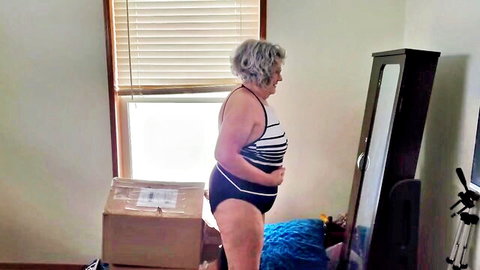 Mature silver-haired curvy woman in striped swimsuit posing sideways