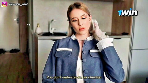 Blonde woman in blue jacket and white gloves standing in kitchen looking serious