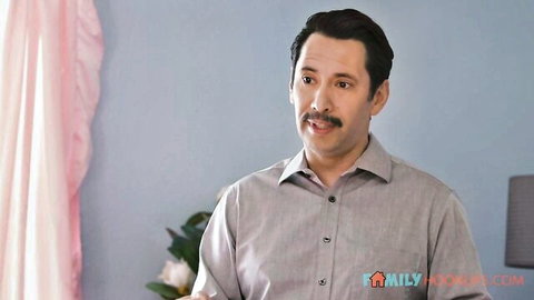 Handsome mustached man in gray shirt smiling seductively in bedroom with pink curtains