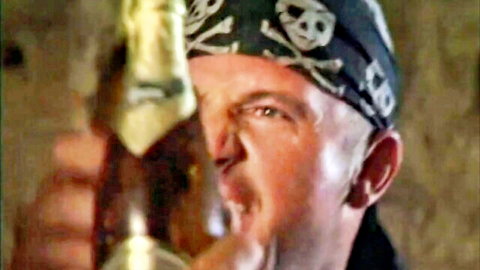 Bald skinhead in pirate bandana holds bottle to mouth intensely
