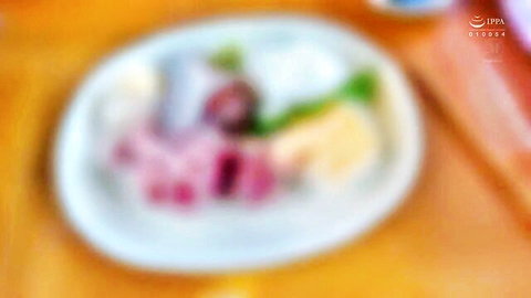 Blurry closeup of pink meat slices, green veggies, yellow bits and white sauce on white plate