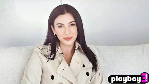 Brunette posing seductively in open trench coat during Playboy interview