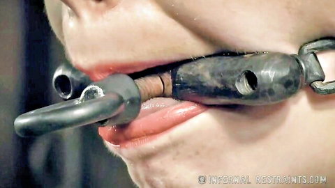 Brunette babe's glossy lips stretched around metal BDSM spider gag in bondage
