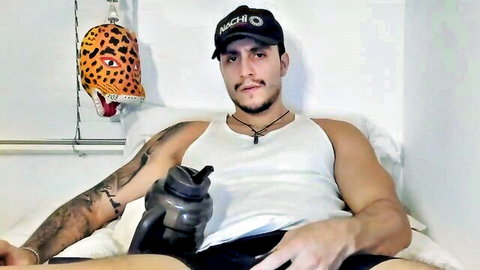 Muscular tattooed hunk smirking in tight white tank top and black shorts on bed