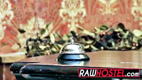 Shiny silver hotel service bell centered on wooden reception desk with ornate red wallpaper background