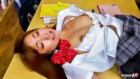 Japanese schoolgirl lies seductively on classroom desk with tits exposed from open white blouse and plaid skirt
