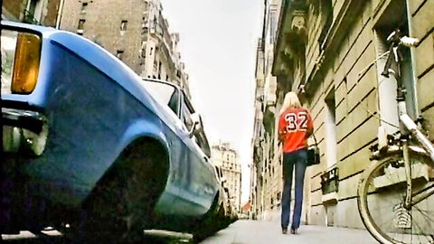 Retro blonde in red jersey #32 walks street near vintage blue car