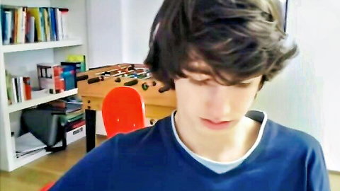 Young shaggy-haired Caucasian guy in blue shirt looks down seductively in solo webcam room