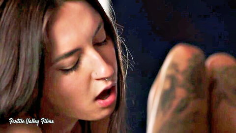 Brunette with nose ring moans open-mouthed against tattooed femdom thighs in lesbian scene