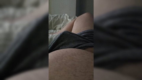 Blurry close-up of mature woman on bed with shorts pulled down, exposing bushy pubic hair, stepmom handjob tease
