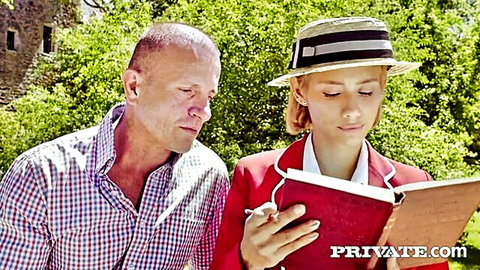 Older bald man stares at young blonde schoolgirl in red blazer hat reading book outdoors