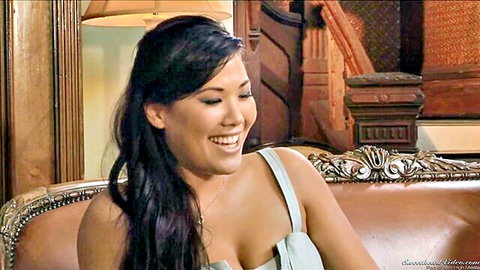 Smiling Asian beauty with deep cleavage in sexy low-cut top on luxury couch