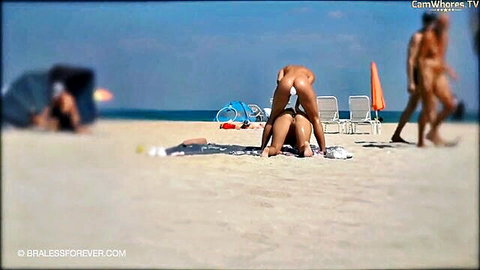 Blonde woman bending over nude on beach with butt plug visible