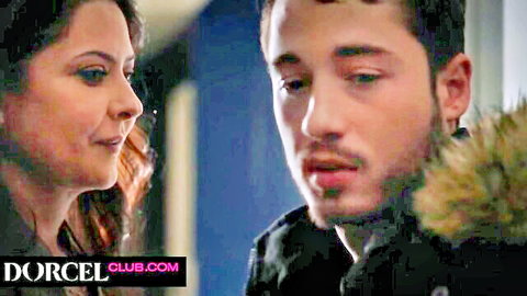 Brunette woman whispers to young bearded man in coats, intimate teaser