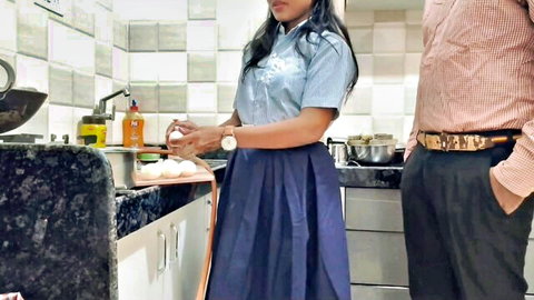 Indian woman in school uniform cutting veggies as man watches in kitchen