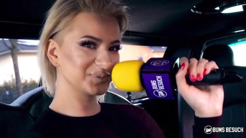 Blonde Dana Jayn holds mic in car, teasing smile for German romance