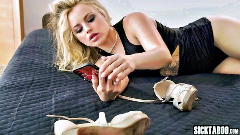 Blonde teen with big tits in black mini dress lies on bed holding phone
