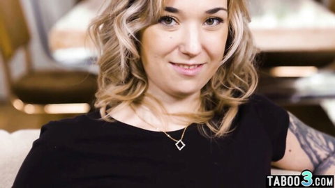 Blonde tattooed woman in black top smiling casually, adult video thumbnail