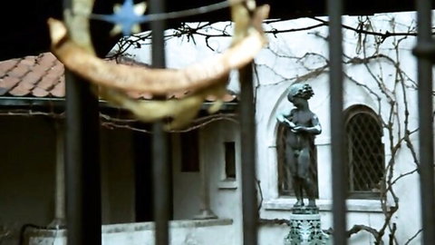 Bronze cherub statue behind ivy-covered wrought iron fence in garden courtyard
