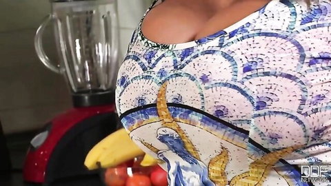 Busty babe with massive oily tits teasing deep cleavage in patterned dress in kitchen near banana and blender