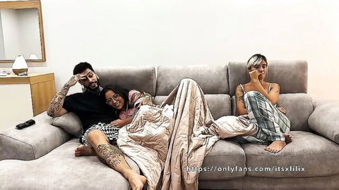 Tattooed guy cuddles busty babes under blanket on couch