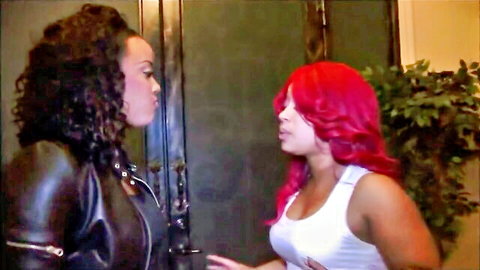 Two sexy ebony babes with curly hair, one in leather jacket and one in tight white tank top, facing intimately.