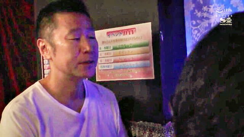 Aroused Asian man in white tee leans close to woman in dim purple-lit Japanese lounge with S1 watermark