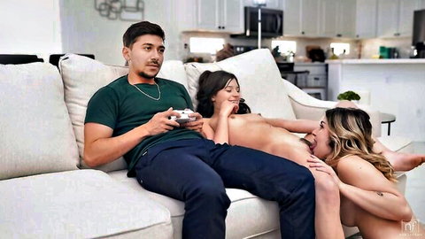 Latino guy plays Xbox on couch with two topless petite women, brunette and blonde exposing small tits