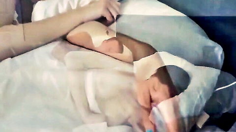 Petite fair-skinned girl with small tits lying in bed holding object near man's head during intimate moment