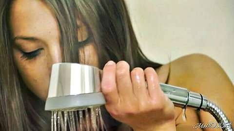 Wet brunette teen holds showerhead to her mouth as water streams over her face and nude shoulders